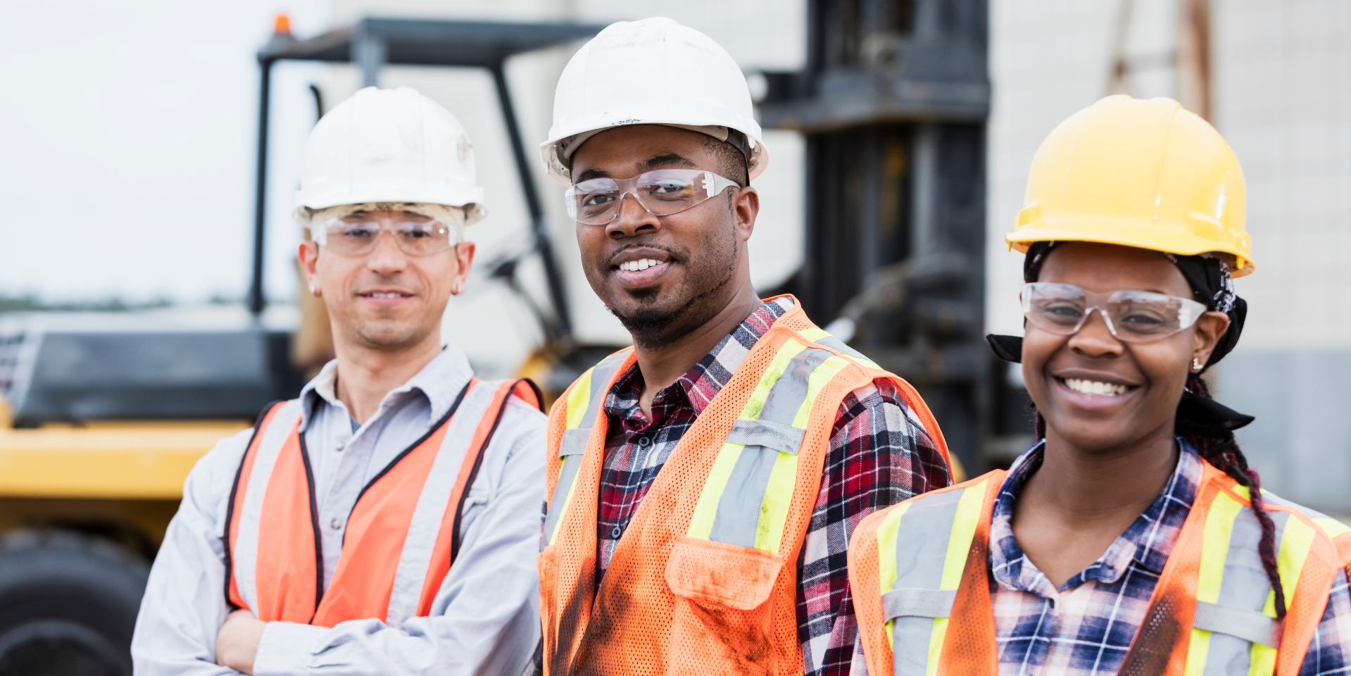 Three construction workers wearing safety vest and hard hats smiling at the camera.